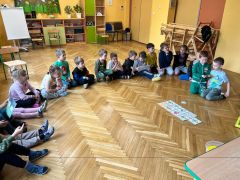 Dzieci siedzą na podłodze i słuchają Pani pszczelarki.