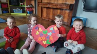 dzieci siedzą na dywanie z papierową laurką w serca