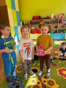 Dziewczynka trzyma laurkę w kształcie cyfry 8, chłopiec trzyma białe tulipany