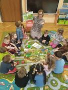 dzieci siedzą w kole na dywanie wraz z nauczycielem