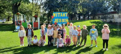 Dzieci pozują na placu zabaw z plakatem Witamy Jesień