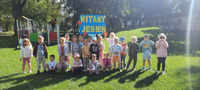 Dzieci pozują na placu zabaw z plakatem Witamy Jesień