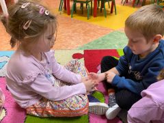 Dzieci siedzi na dywanie i wykonuje sobie nawzajem masażyki