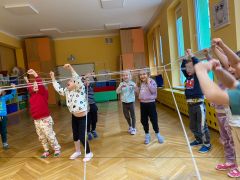 Dzieci stoją w sali i trzymają sznurki uniesione do góry
