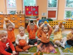 Dzieci siedzą na dywanie i trzymają dynie