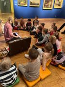 Dzieci siedzą w półkolu i słuchają Pani prowadzącej.