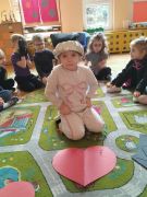 Dziewczynka siedzi przed dużym papierowym sercem na dywanie.