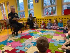 Dzieci siedzą w kole i słuchają Pana ze Straży Miejskiej.