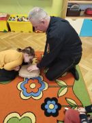 Dziewczynka wykonuje resuscytację na manekinie pod okiem strażnika miejskiego.