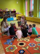 Dzieci siedzą na dywanie i słuchają studentki Stomatologii.