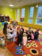 Dzieci siedzą na dywanie i słuchają studentki Stomatologii.