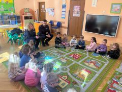 Dzieci siedzą na dywanie, słuchają policjantów.