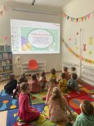 Dzieci siedzą na dywanie i oglądają prezentację.