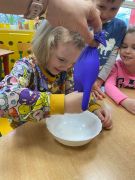 Dziewczynka ściska rękawiczkę z której wypływa mleko.