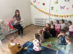 Dzieci siedzą na dywanie i słuchają Pani.