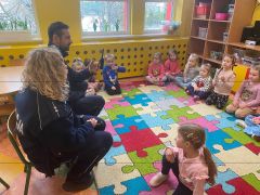 Dzieci siedzą na dywanie i słuchają policjantów.